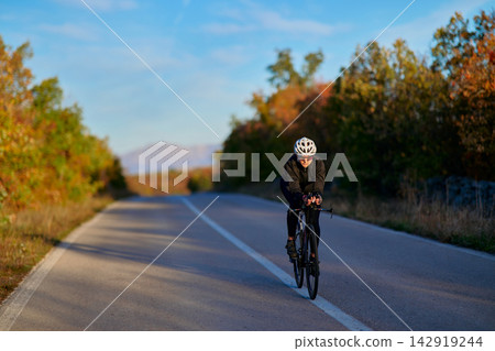 Road Cyclist Training on Open Country Highway in Autumn Wearing Helmet and Cycling Gear Road Cyclist Training on Open Country Highway in Autumn Wearing Helmet and Cycling Gear 142919244