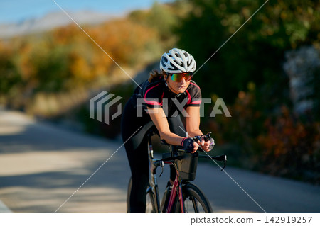 Female Cyclist Training on Road Bike in Aerodynamic Position During Sunny Autumn Ride Female Cyclist Training on Road Bike in Aerodynamic Position During Sunny Autumn Ride 142919257