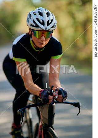 Female Cyclist in Aerodynamic Position Wearing Helmet and Mirrored Sunglasses on Road Bike 142919267