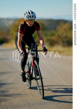 Female Cyclist Training on Road Bike Wearing Helmet and Sunglasses During Outdoor Fitness Ride Female Cyclist Training on Road Bike Wearing Helmet and Sunglasses During Outdoor Fitness Ride 142919269