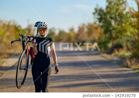Female Cyclist Carrying Road Bike on Rural Road During Sunny Autumn Training Session 142919270