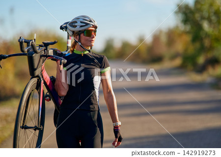Female Cyclist Carrying Road Bike On Shoulder During Training Ride On Rural Road At Sunset Female Cyclist Carrying Road Bike On Shoulder During Training Ride On Rural Road At Sunset 142919273