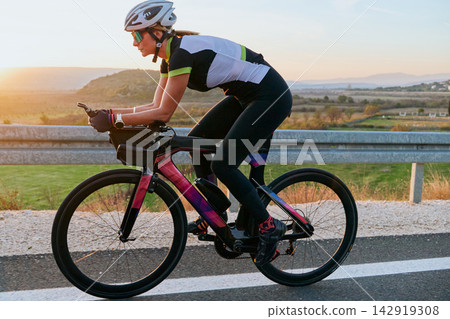Female Cyclist Training on Road Bike at Sunrise Triathlon Athlete Cycling Workout Outdoors 142919308