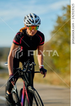 Female Cyclist Training on Road Bike Outdoors Wearing Helmet and Performance Sunglasses at Speed Female Cyclist Training on Road Bike Outdoors Wearing Helmet and Performance Sunglasses at Speed 142919325