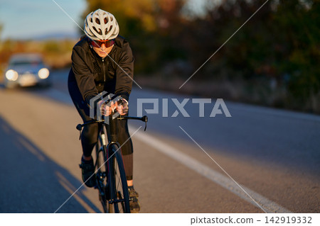 Road Cyclist Riding Fast on Country Road at Sunset Wearing Helmet and Cycling Gear Road Cyclist Riding Fast on Country Road at Sunset Wearing Helmet and Cycling Gear 142919332