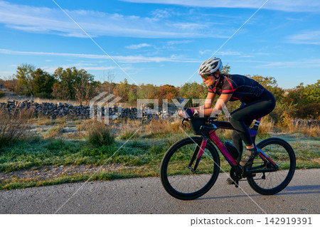 Female Cyclist Training on Road Bike Outdoors at Sunrise - Fitness Cycling Athlete Riding Female Cyclist Training on Road Bike Outdoors at Sunrise - Fitness Cycling Athlete Riding 142919391