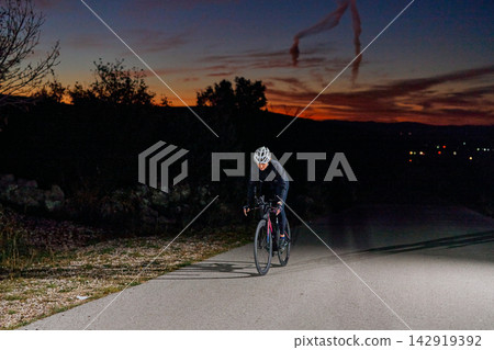 Night Road Cyclist Training At Sunset Wearing Helmet And Reflective Gear On Empty Country Road Night Road Cyclist Training At Sunset Wearing Helmet And Reflective Gear On Empty Country Road 142919392