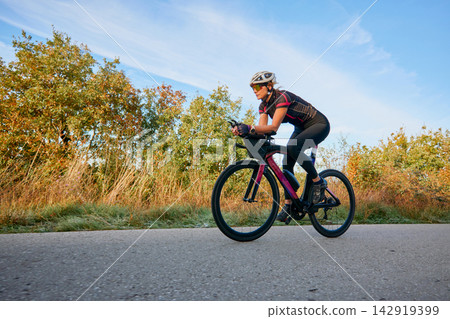 Female Cyclist Training On Road Bike During Sunrise Outdoor Fitness Ride In Autumn Countryside Female Cyclist Training On Road Bike During Sunrise Outdoor Fitness Ride In Autumn Countryside 142919399