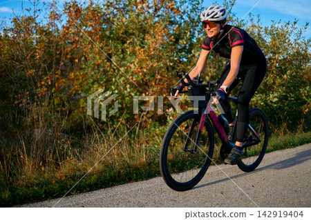 Female Cyclist Riding Road Bike Outdoors for Fitness Training on Sunny Autumn Day 142919404