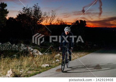 Solo Road Cyclist Training at Sunset on Rural Roadside During Nighttime Endurance Ride Solo Road Cyclist Training at Sunset on Rural Roadside During Nighttime Endurance Ride 142919408