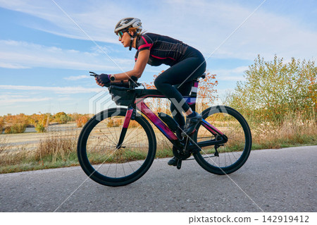 Female Cyclist Riding Aerodynamic Road Bike Outdoors at Sunrise Training for Triathlon and Fitness Female Cyclist Riding Aerodynamic Road Bike Outdoors at Sunrise Training for Triathlon and Fitness 142919412