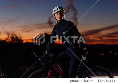 Female Cyclist Training On Road Bike At Sunset Wearing Helmet And Cycling Gear 142919413