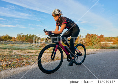 Female Cyclist Training on Road Bike at Sunrise With Aerodynamic Helmet and Sunglasses Female Cyclist Training on Road Bike at Sunrise With Aerodynamic Helmet and Sunglasses 142919417