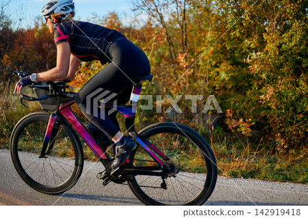 Female Cyclist Training on Aerodynamic Road Bike in Autumn Countryside During Outdoor Fitness Ride Female Cyclist Training on Aerodynamic Road Bike in Autumn Countryside During Outdoor Fitness Ride 142919418
