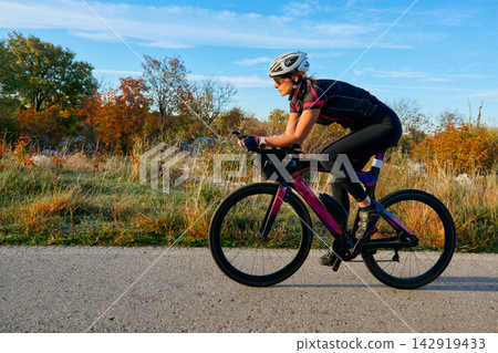 Female Cyclist Riding Aero Road Bike Outdoors at Sunset Training for Fitness and Endurance Female Cyclist Riding Aero Road Bike Outdoors at Sunset Training for Fitness and Endurance 142919433