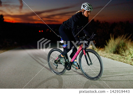 Female Cyclist Training on Road Bike at Dusk Night Ride for Fitness and Endurance Female Cyclist Training on Road Bike at Dusk Night Ride for Fitness and Endurance 142919443