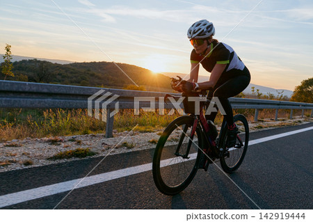 Female Cyclist Training on Road Bike at Sunset During Outdoor Cycling Workout for Triathlon 142919444