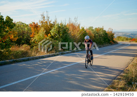 Solo Cyclist Riding Road Bike On Scenic Autumn Country Road With Trees And Distant Hills Solo Cyclist Riding Road Bike On Scenic Autumn Country Road With Trees And Distant Hills 142919450