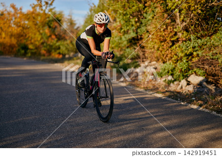 Focused Road Cyclist Training on Country Road Surrounded by Autumn Foliage for Fitness and Endurance Focused Road Cyclist Training on Country Road Surrounded by Autumn Foliage for Fitness and Endurance 142919451