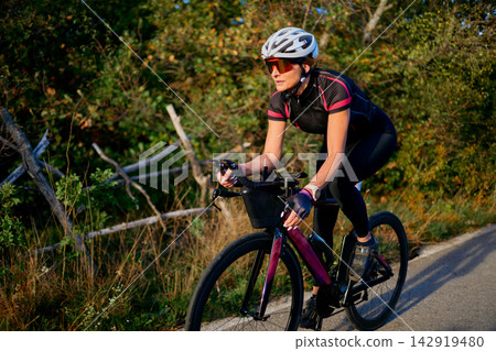 Female Cyclist Training On Country Road At Sunset Wearing Helmet And Cycling Gear Female Cyclist Training On Country Road At Sunset Wearing Helmet And Cycling Gear 142919480