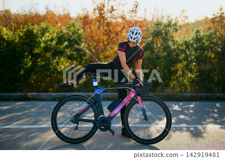 Female Cyclist Preparing on High-Performance Triathlon Bike During Outdoor Road Training Session Female Cyclist Preparing on High-Performance Triathlon Bike During Outdoor Road Training Session 142919481