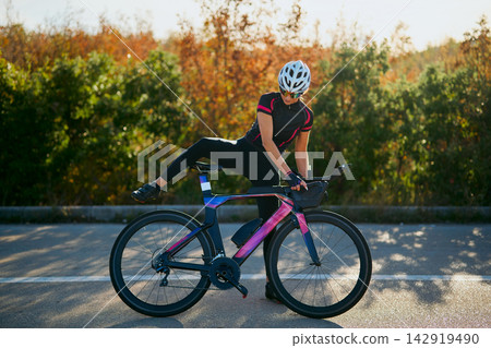 Female Cyclist Mounting Aerodynamic Road Bike On Quiet Sunlit Road During Training Ride Female Cyclist Mounting Aerodynamic Road Bike On Quiet Sunlit Road During Training Ride 142919490