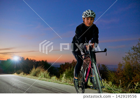 Female Cyclist Training On Rural Road At Dusk With Helmet And Racing Bicycle Female Cyclist Training On Rural Road At Dusk With Helmet And Racing Bicycle 142919556
