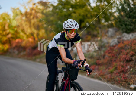 Female Cyclist Riding Road Bike on Country Road During Autumn Training Session Outdoors Scenic 142919580