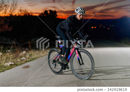Female Cyclist Riding Road Bike At Sunset On Rural Road During Evening Training 142919619