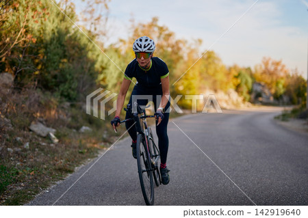Female Road Cyclist Training on Winding Country Road at Sunrise in Autumn Cycling Kit Female Road Cyclist Training on Winding Country Road at Sunrise in Autumn Cycling Kit 142919640