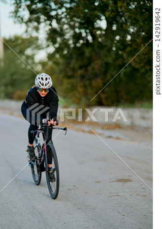 Female Cyclist Riding Road Bike in Aerodynamic Position on Quiet Country Road Female Cyclist Riding Road Bike in Aerodynamic Position on Quiet Country Road 142919642