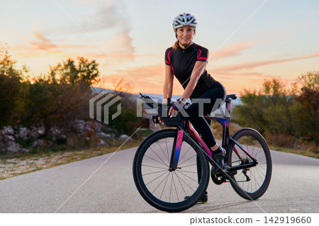 Female Cyclist On Road Bike Training At Sunset On Rural Country Road 142919660