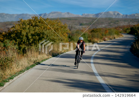Solo Road Cyclist Training Through Scenic Mountain Landscape On Winding Asphalt Road Solo Road Cyclist Training Through Scenic Mountain Landscape On Winding Asphalt Road 142919664