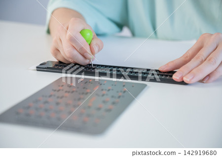 A blind woman writes in Braille using a stencil on a piece of paper.  142919680
