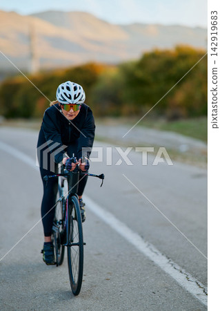 Female Cyclist Training on Open Road in Autumn Landscape With Helmet and Aero Bike Female Cyclist Training on Open Road in Autumn Landscape With Helmet and Aero Bike 142919683