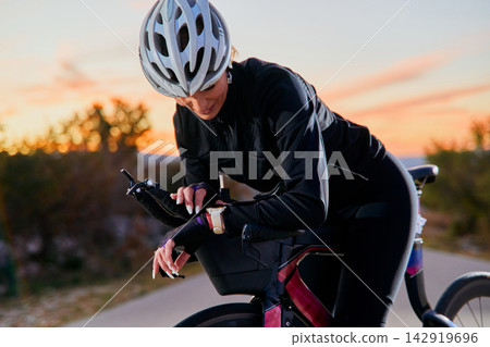 Female Cyclist Checking Smartwatch On Aero Triathlon Bike During Sunset Training Ride Female Cyclist Checking Smartwatch On Aero Triathlon Bike During Sunset Training Ride 142919696