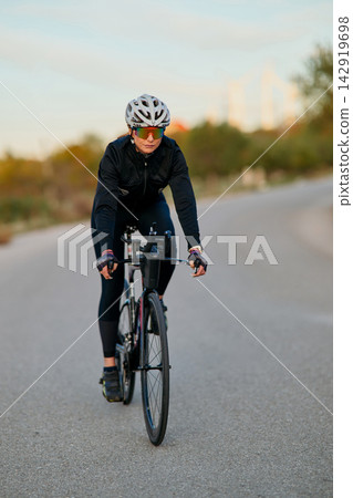 Female Cyclist Training on Road Bike at Sunrise Wearing Helmet and Sunglasses for Fitness Female Cyclist Training on Road Bike at Sunrise Wearing Helmet and Sunglasses for Fitness 142919698