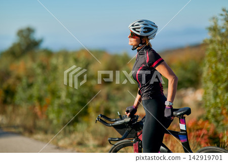 Female Cyclist Pausing With Road Bike Wearing Helmet and Sportswear On Scenic Outdoor Trail Female Cyclist Pausing With Road Bike Wearing Helmet and Sportswear On Scenic Outdoor Trail 142919701