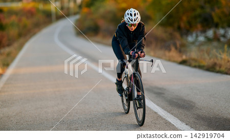 Female Cyclist Riding Road Bike On Winding Country Road During Autumn Training Session Female Cyclist Riding Road Bike On Winding Country Road During Autumn Training Session 142919704