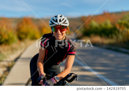 Female Cyclist Smiling On Road Bike Wearing Helmet And Sunglasses In Autumn Outdoors Female Cyclist Smiling On Road Bike Wearing Helmet And Sunglasses In Autumn Outdoors 142919705