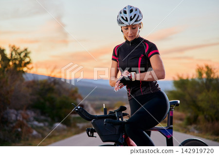 Female Cyclist Checking Smartwatch During Sunset Road Bike Training Ride For Fitness And Endurance Female Cyclist Checking Smartwatch During Sunset Road Bike Training Ride For Fitness And Endurance 142919720