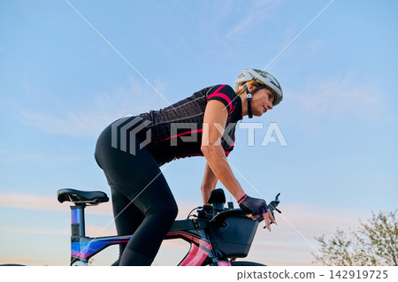 Female Cyclist Riding Road Bike at Sunset Wearing Helmet and Cycling Gear for Fitness Training Female Cyclist Riding Road Bike at Sunset Wearing Helmet and Cycling Gear for Fitness Training 142919725