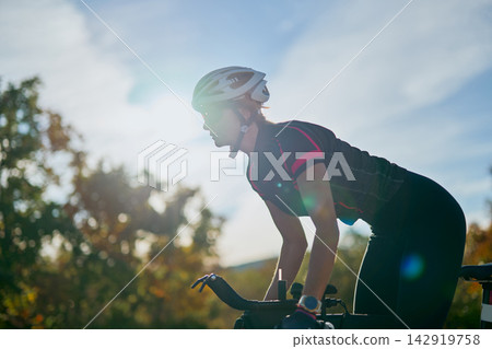 Female Cyclist Training Outdoors at Sunset on Road Bike Wearing Helmet and Athletic Gear Female Cyclist Training Outdoors at Sunset on Road Bike Wearing Helmet and Athletic Gear 142919758