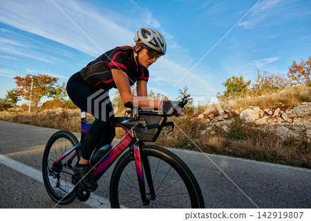 Female Cyclist Training On A Road Bike During Outdoor Time Trial Ride At Sunset Female Cyclist Training On A Road Bike During Outdoor Time Trial Ride At Sunset 142919807