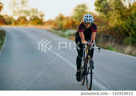 Female Road Cyclist Training on Country Road at Sunrise Showing Fitness, Focus and Endurance Female Road Cyclist Training on Country Road at Sunrise Showing Fitness, Focus and Endurance 142919813