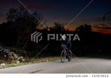 Solo Cyclist Training on a Country Road at Dusk Nightfall Wearing Helmet and Cycling Gear 142919818