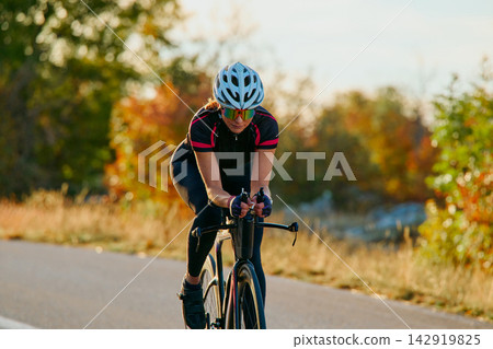 Female Road Cyclist Training On Bike In Autumn Countryside Wearing Helmet And Sunglasses Female Road Cyclist Training On Bike In Autumn Countryside Wearing Helmet And Sunglasses 142919825