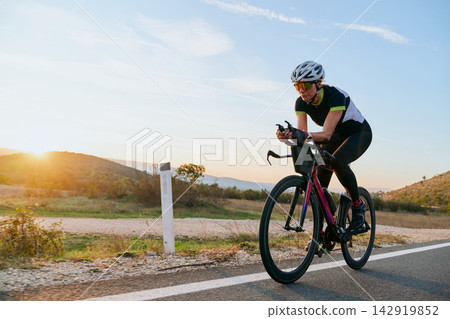 Female Cyclist Training on Road Bike at Sunrise Along Country Road During Outdoor Endurance Ride Female Cyclist Training on Road Bike at Sunrise Along Country Road During Outdoor Endurance Ride 142919852