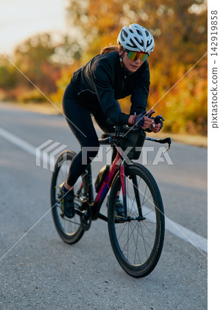 Female Cyclist Training on Road Bike at Sunrise in Autumn Triathlon Time Trial Athlete Female Cyclist Training on Road Bike at Sunrise in Autumn Triathlon Time Trial Athlete 142919858