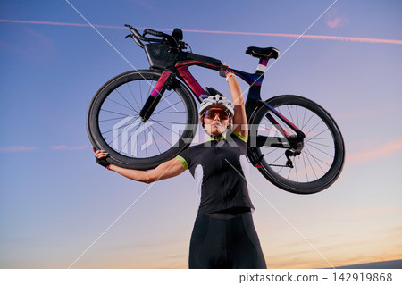 Triathlete Cyclist Lifting Road Bike Overhead At Sunrise Celebrating Strength And Victory Triathlete Cyclist Lifting Road Bike Overhead At Sunrise Celebrating Strength And Victory 142919868